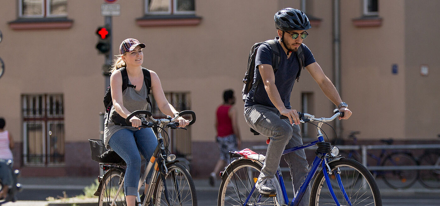 Das Bild zeigt zwei jungen Menschen, die in der Stadt radeln